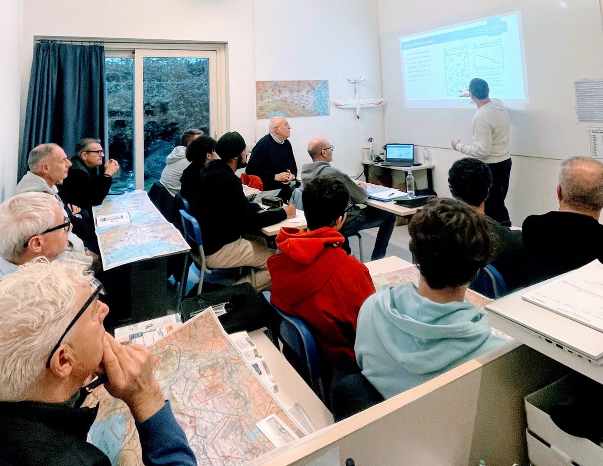 Gli allievi seduti in aula durante una lezione di teoria, con le carte aeronautiche sui tavoli