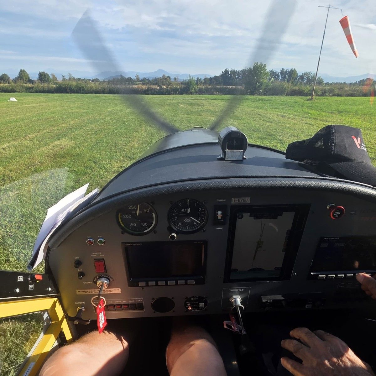 Cruscotto del Tecnam P92 con istruttore ai comandi, davanti la pista in erba