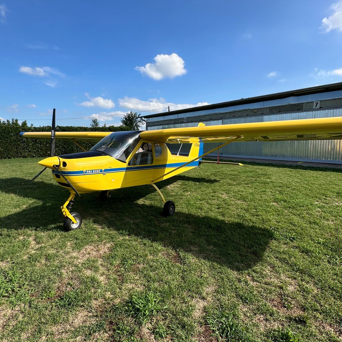 Il Tecnam P92 Echo giallo della scuola parcheggiato sul prato davanti all'hangar